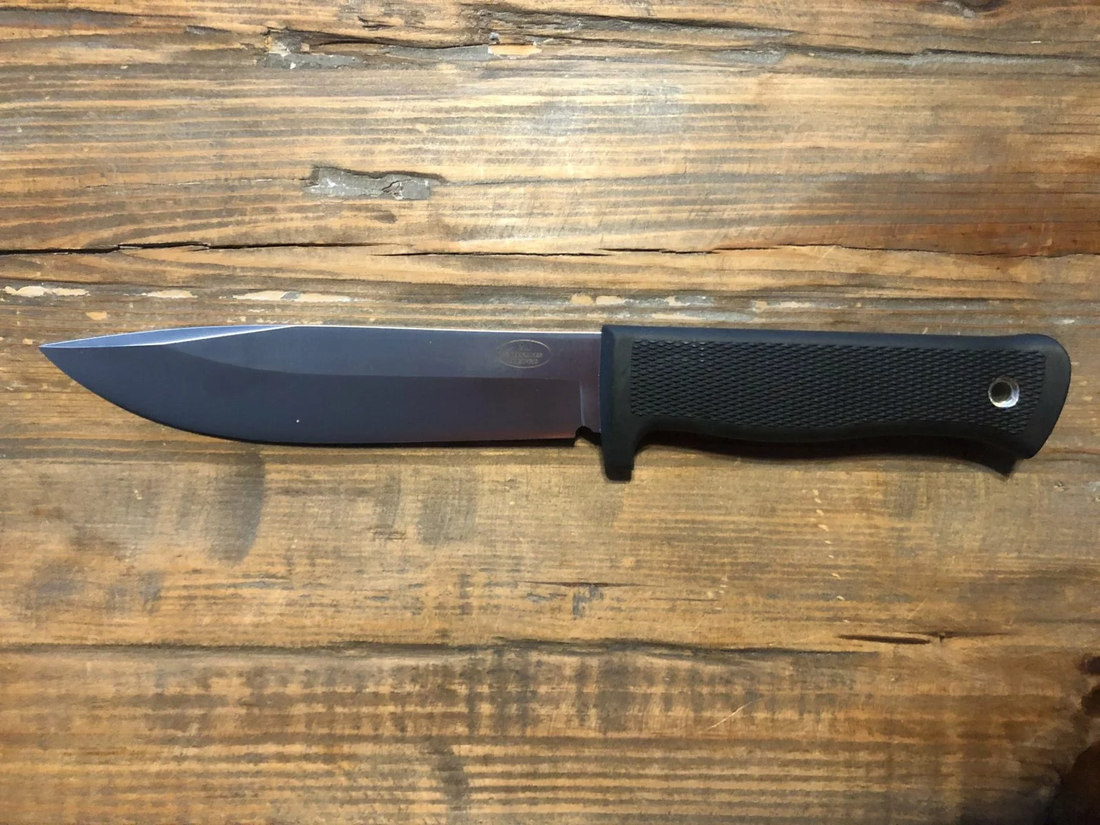 Couteau Fällkniven A1 à lame fixe et manche noir quadrillé, posé sur une table en bois