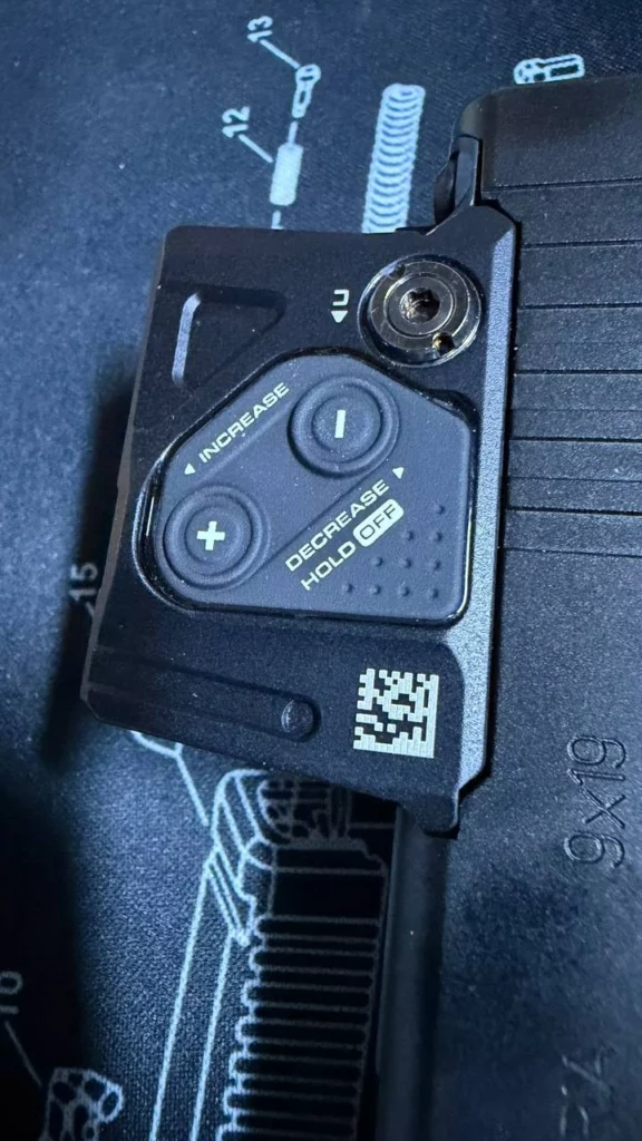 Flanc de l'Aimpoint COA avec ses boutons plus et moins pour l'intensité et la vis de réglage en hauteur.