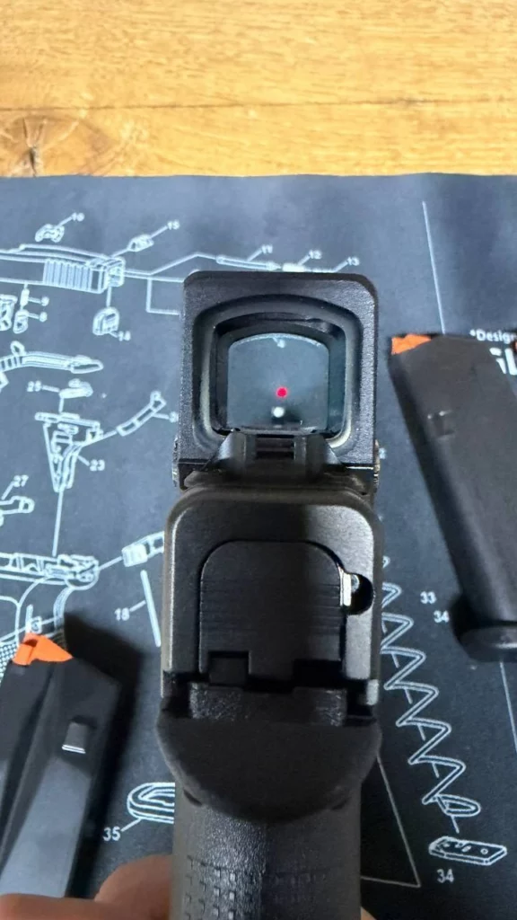 Vue arrière d'un Glock 43X avec le point rouge Aimpoint COA allumé dans la fenêtre, chargeurs autour.