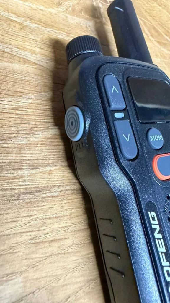 Gros plan sur le côté d'un talkie-walkie Baofeng, avec le bouton PTT latéral, la molette et l'antenne courte.