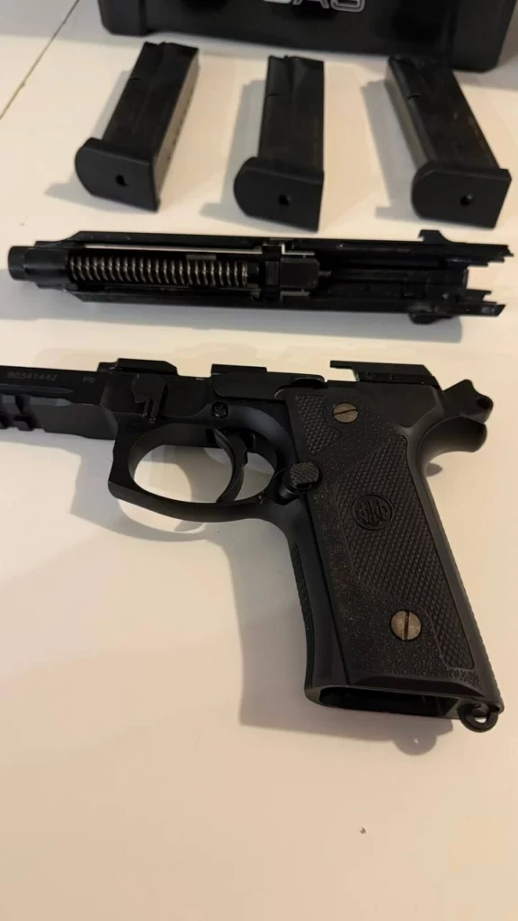 Beretta M9A3 démonté : culasse avec canon et ressort récupérateur au-dessus de la carcasse, trois chargeurs au fond.