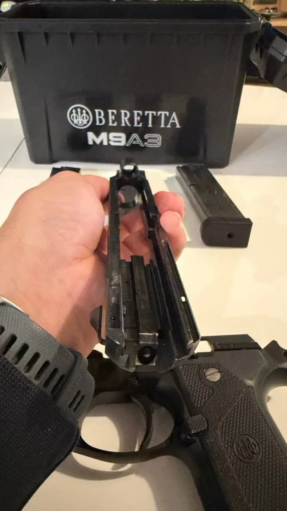 Culasse du Beretta M9A3 vue de dessous, tenue à la main au-dessus de la carcasse.