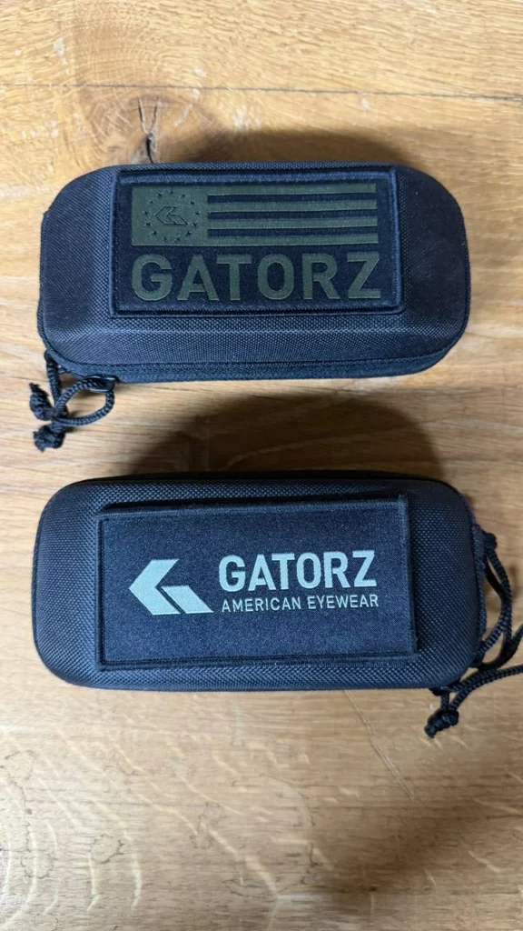 Deux étuis noirs Gatorz, l'un avec un écusson drapeau américain kaki, l'autre avec le logo American Eyewear.