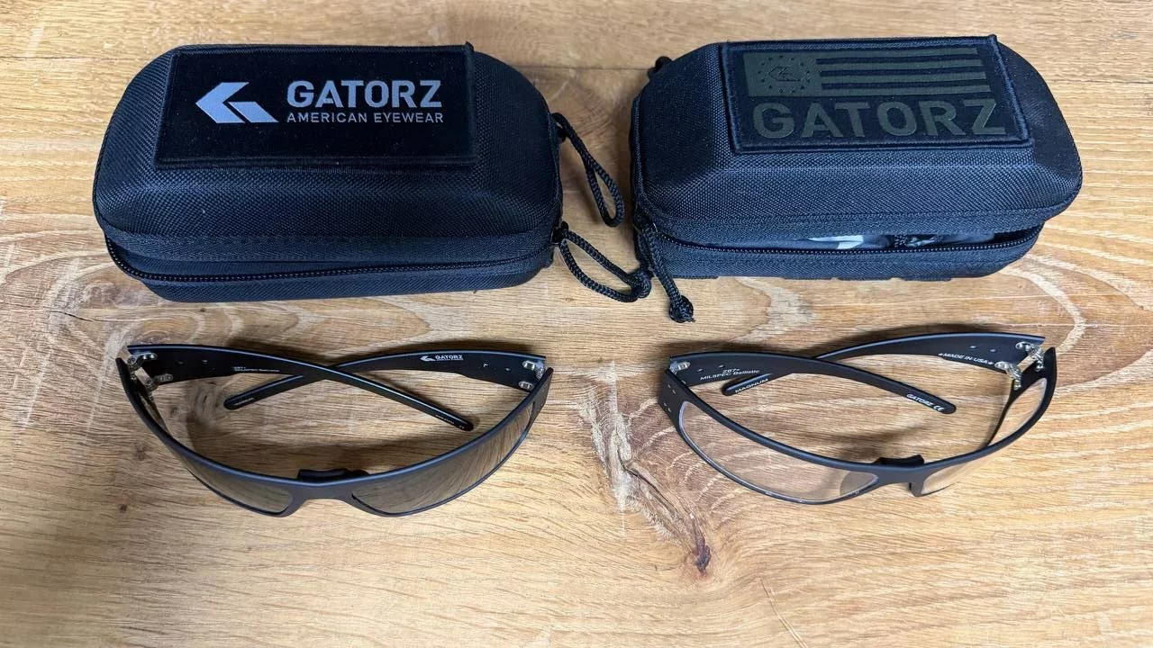 Deux paires de lunettes Gatorz, verres clairs et verres fumés, posées à côté de leurs étuis noirs sur une table en bois.