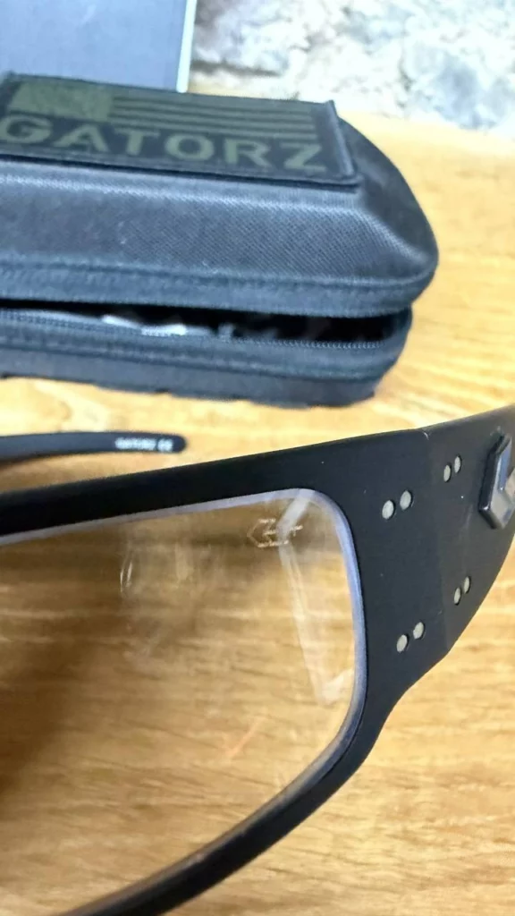 Détail de la monture Gatorz en aluminium noir avec ses rivets, devant un étui à écusson kaki.