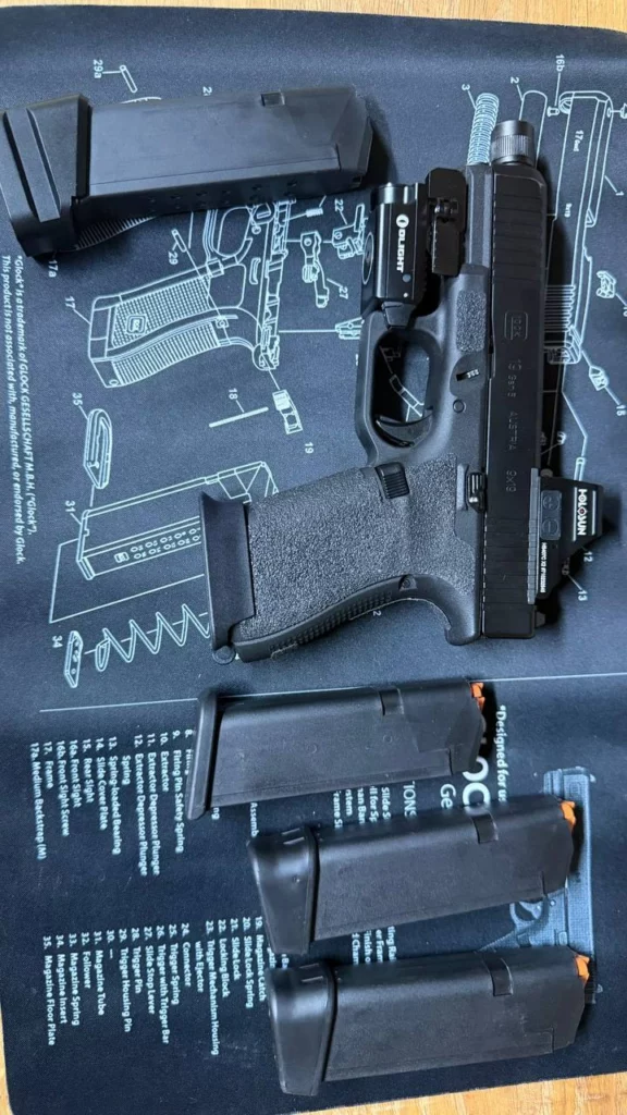 Glock 19 Gen5 avec point rouge Holosun et lampe Olight, posé sur un tapis de nettoyage à côté de quatre chargeurs.