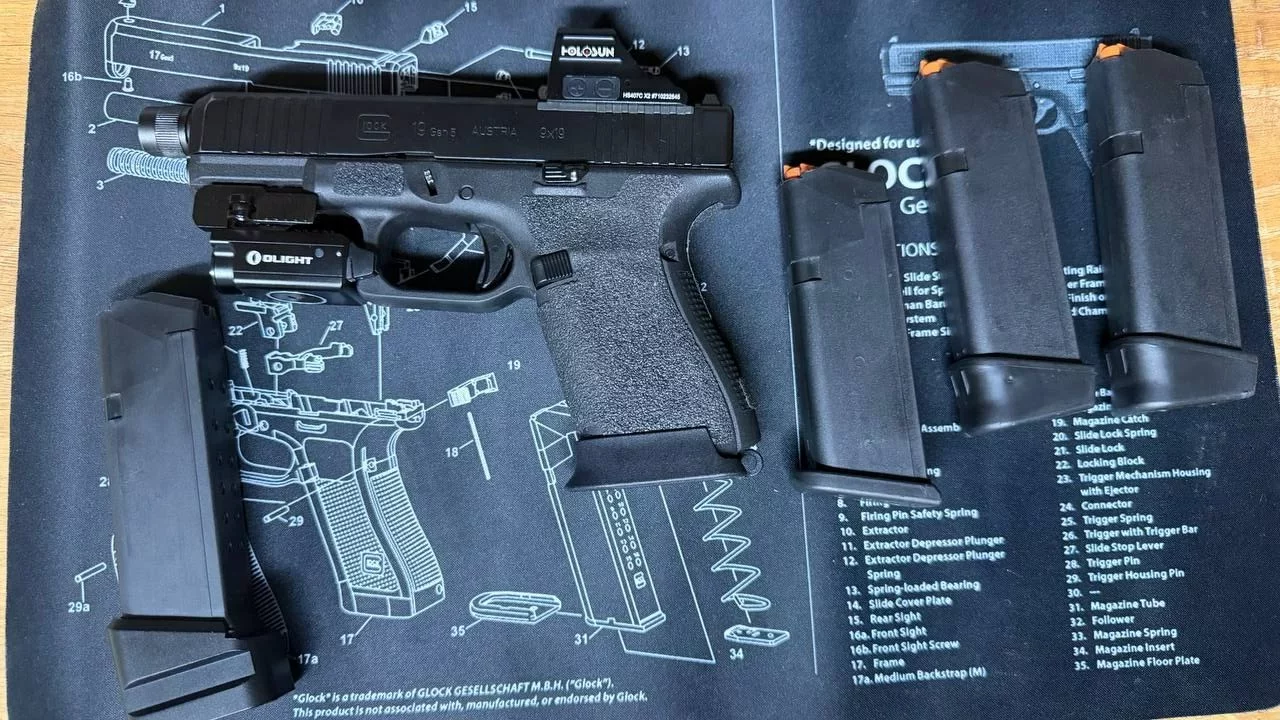 Glock 19 Gen5 avec point rouge Holosun et lampe Olight, posé sur un tapis de nettoyage à côté de quatre chargeurs.