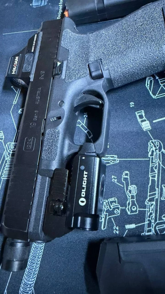 Flanc gauche du Glock 19 Gen5, avec le point rouge Holosun sur la culasse et la lampe Olight sur le rail.