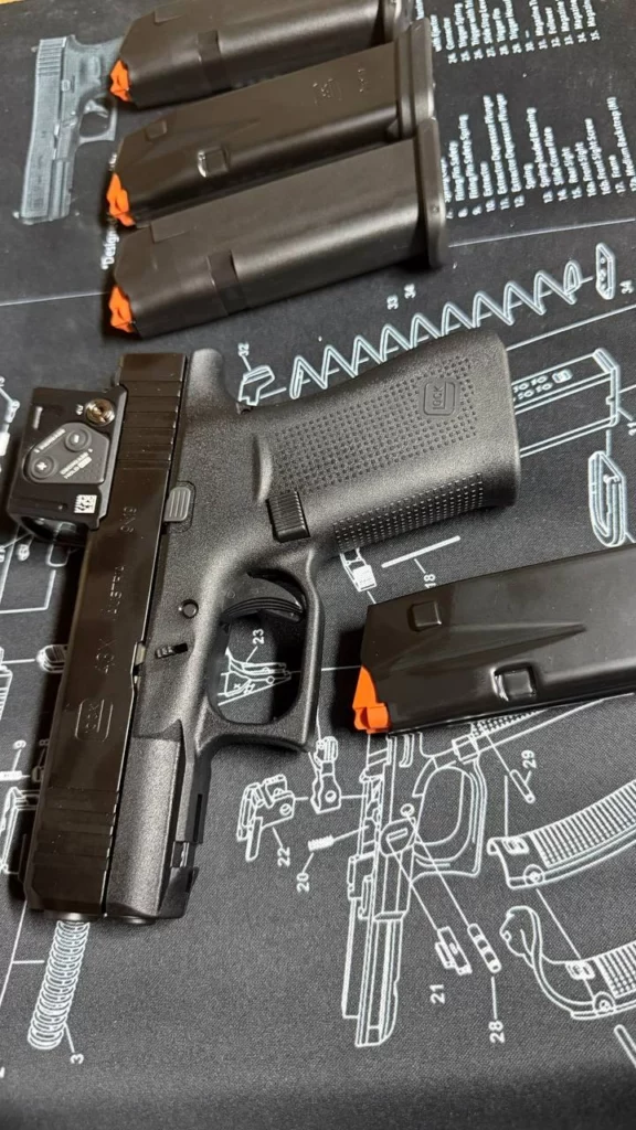 Glock 43X avec point rouge, vu de côté sur un tapis d'entretien, avec plusieurs chargeurs à élévateur orange.