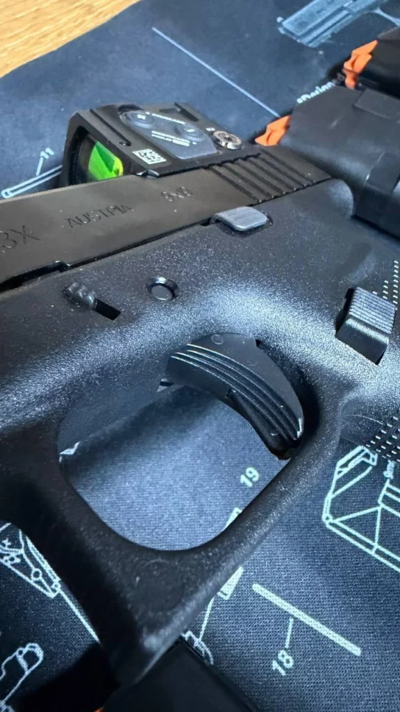 Gros plan sur la détente et le pontet du Glock 43X, avec le point rouge en arrière-plan.