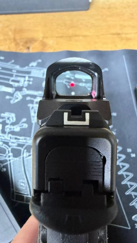 Vue de derrière d'un pistolet équipé d'un Holosun HS407C X2, point rouge allumé dans la fenêtre et hausse visible dessous.