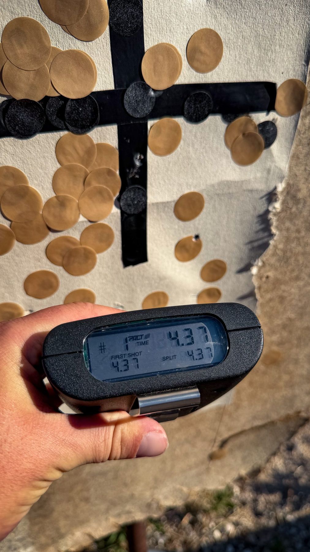 Chronomètre de tir tenu en main devant une cible criblée d'impacts