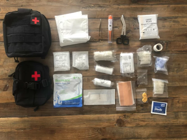 Contenu d'une trousse de secours étalé sur une table en bois, à côté de deux pochettes noires
