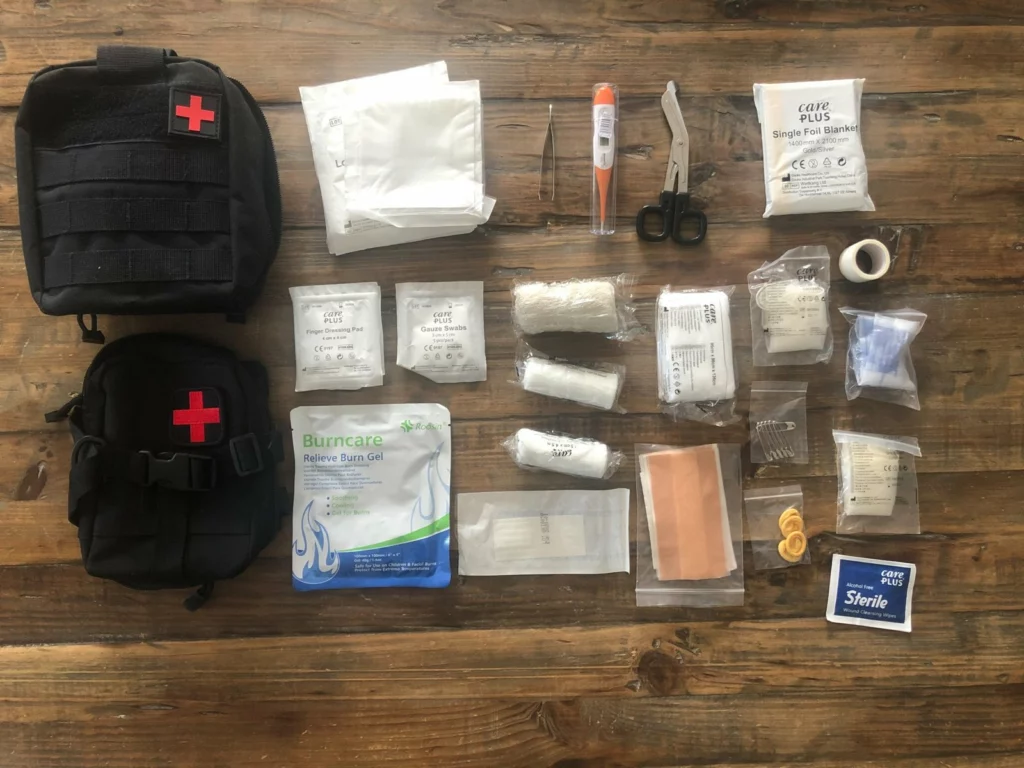 Contenu de la trousse étalé sur une table : compresses, bandes, gel pour brûlures, ciseaux, thermomètre, couverture de survie